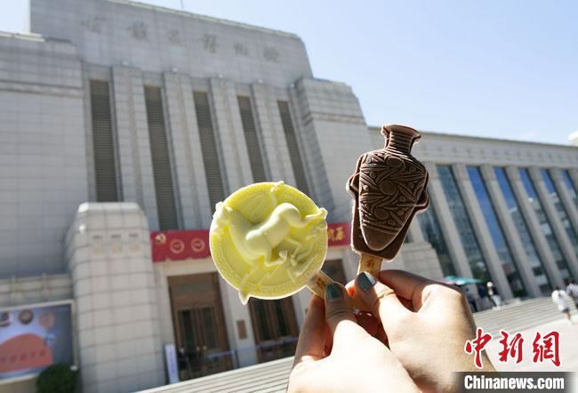 2021年7月30日，游客手拿“铜奔马”“彩陶瓶”造型的雪糕，在甘肃省博物馆前拍照打卡。　高展 摄